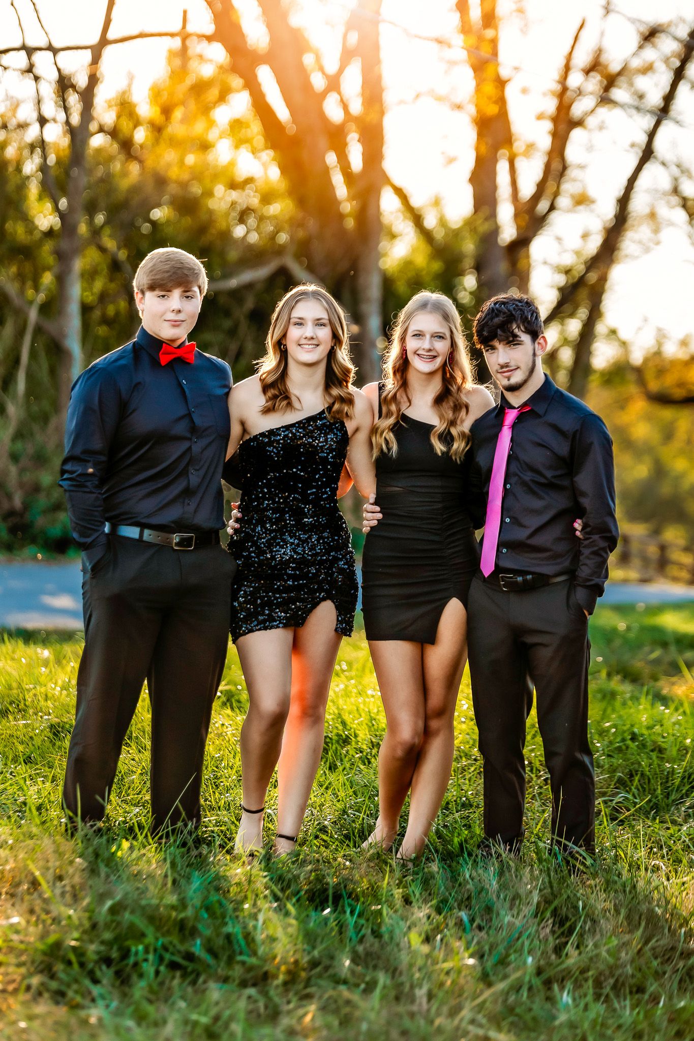 Group photo of friends in formal attire standing in a grassy field at golden hour.