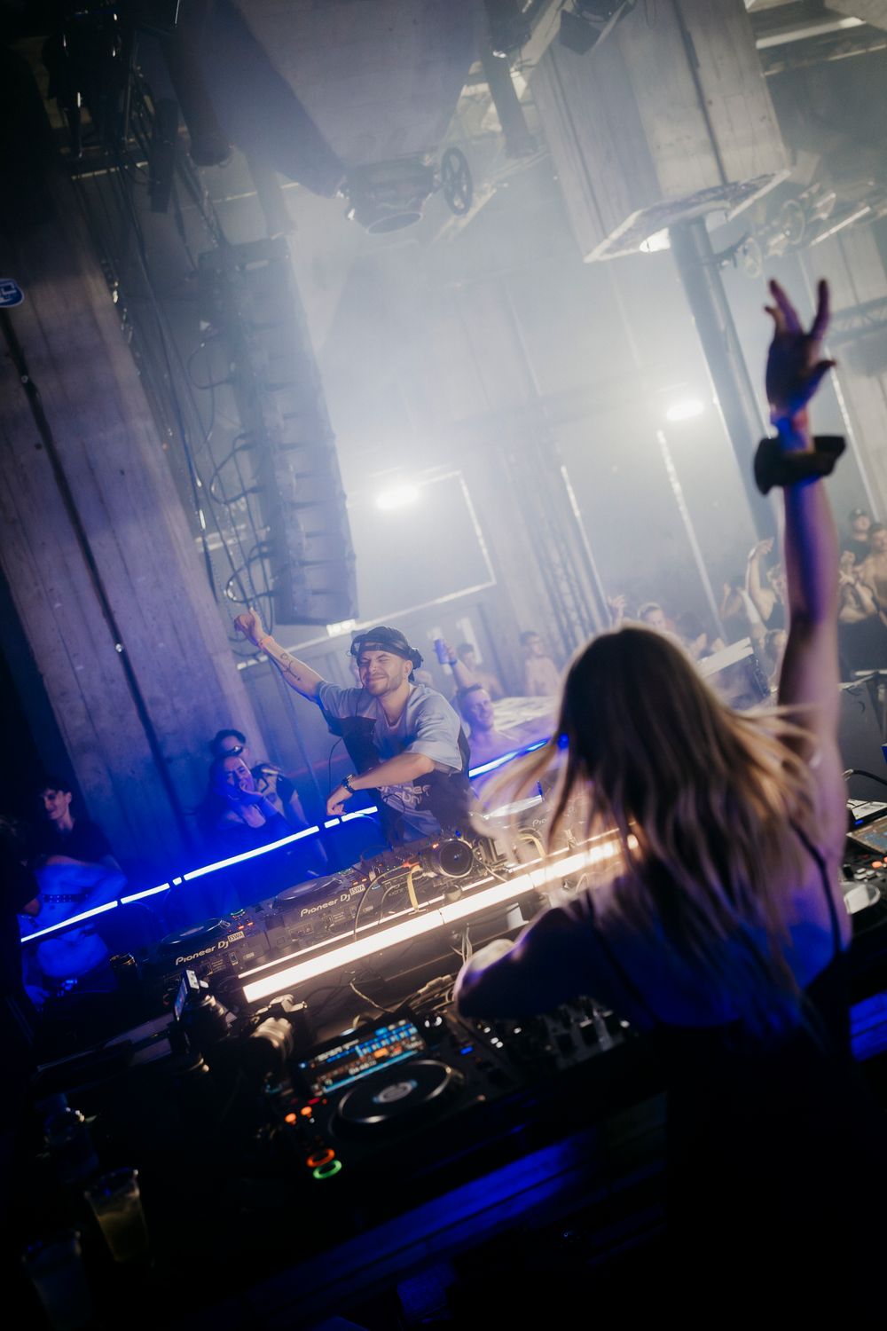 Concert crowd silhouettes with blue laser lights and fog creating an energetic nightclub atmosphere.