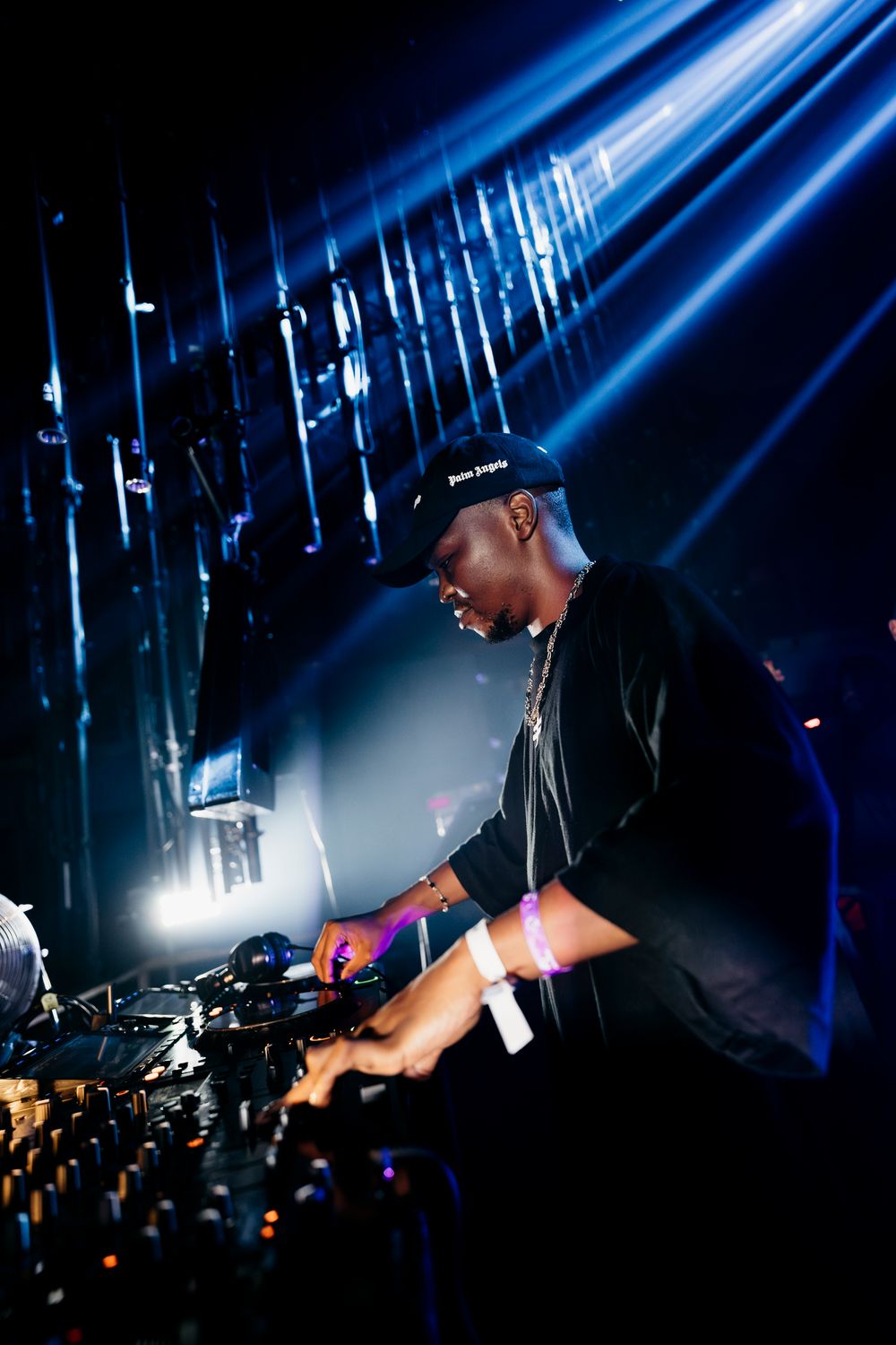 DJ performing at a concert with bright blue spotlights streaming down.