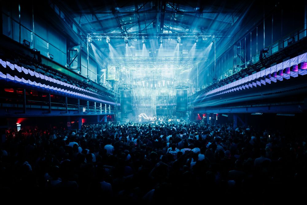 Wide panorama of a packed nightclub with blue lighting and laser effects.