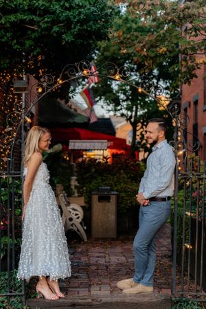 A romantic moment captured under an ornate iron archway with twinkling lights and garden scenery.