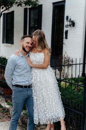 A couple shares a joyful moment outside a white building with black trim.