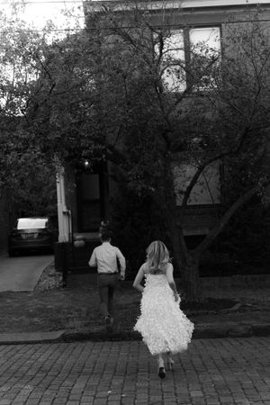 A couple walks away from camera on a brick path in black and white photography.