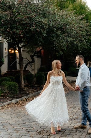 A couple dances on a cobblestone street as her white dress twirls around her.