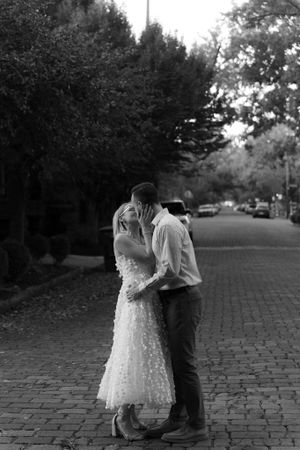 A romantic black and white photo of a couple embracing on a cobblestone street.