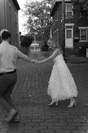 A playful couple dances and holds hands on a brick-paved street.