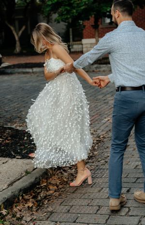 A couple dances playfully on a cobblestone sidewalk near autumn trees.