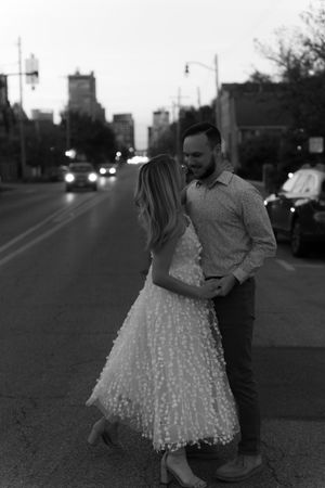 A black and white romantic street scene with city lights and buildings in the background.