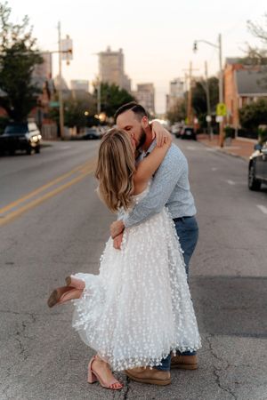 A romantic dip kiss captured at sunset on a city street with urban buildings in the background.