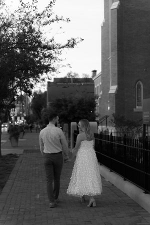 A black and white image of a couple walking along a brick path beside a historic church.