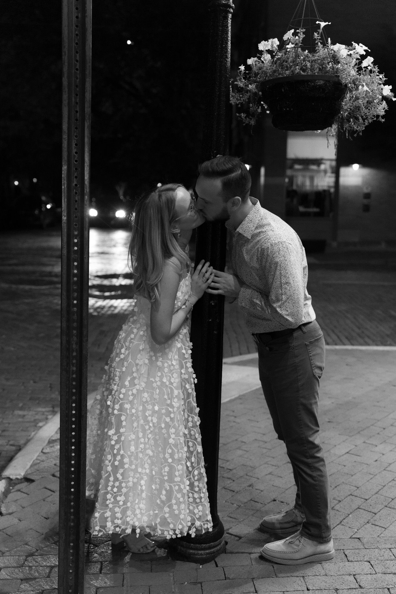 Romantic nighttime moment under a hanging flower basket on a brick street corner.