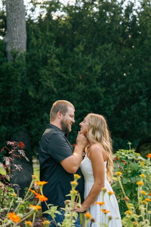 A romantic couple embraces in a garden with bright orange flowers and lush greenery in the background.