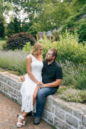 A couple shares an intimate moment while sitting on a stone wall surrounded by lavender and garden flowers.