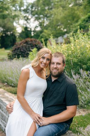 A couple poses together on a garden path surrounded by blooming lavender and greenery.