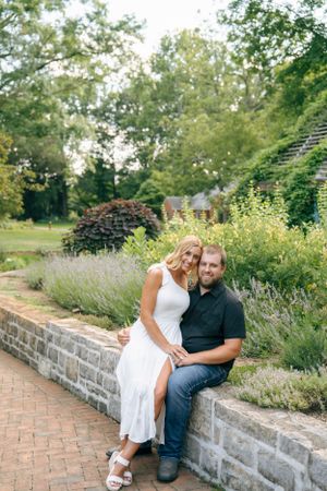 A couple sits together on a stone wall in a beautiful garden setting with lavender flowers.