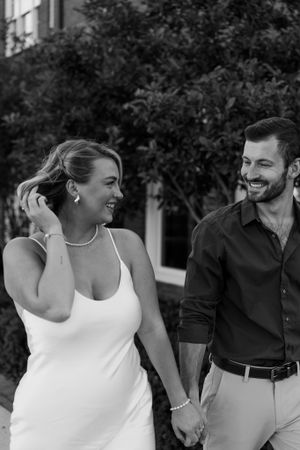 A black and white portrait of a couple laughing together while holding hands outdoors.