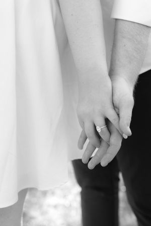 Close-up black and white photo of hands clasped together, showing an engagement ring.