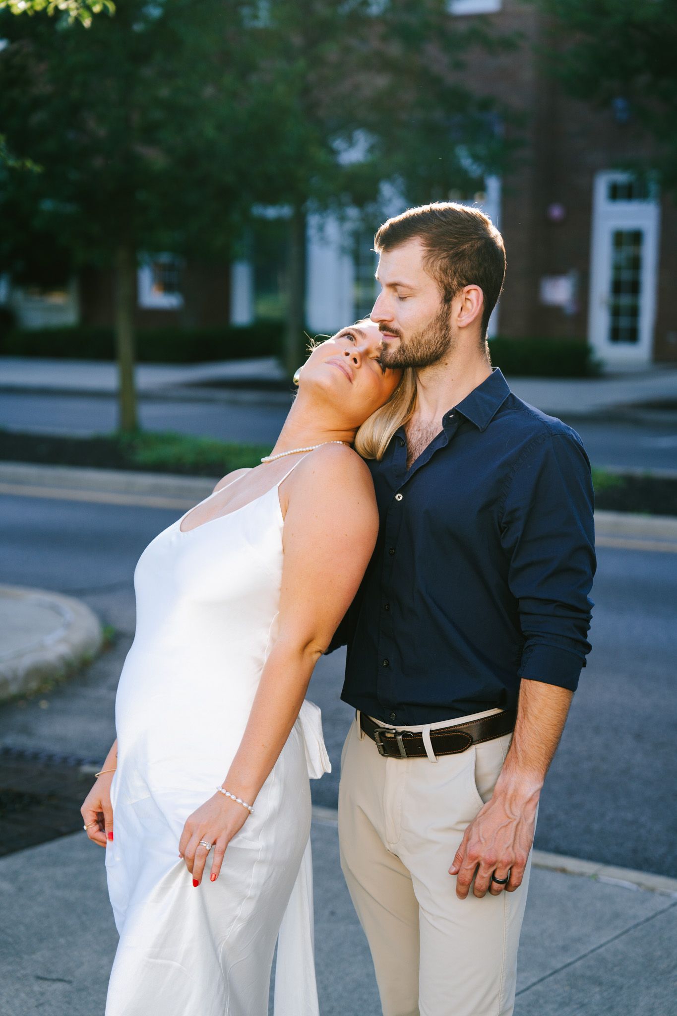 A romantic couple shares a tender moment on an urban street corner at dusk.