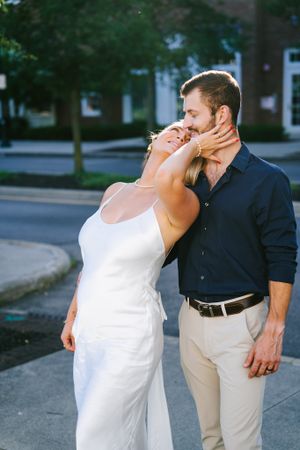 A couple in contrasting outfits shares a passionate embrace on a city street.