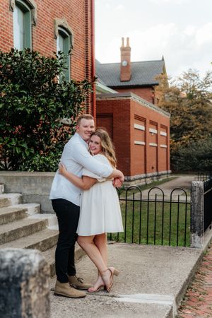 A couple shares an intimate moment on brick steps outside a historic building.