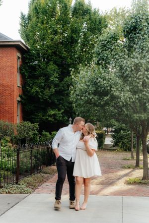 A romantic couple shares a tender moment while walking on a brick sidewalk.