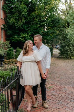 A couple walks hand in hand along an iron-fenced brick pathway.