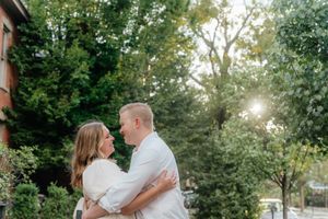 A couple embraces in golden evening light surrounded by green trees.