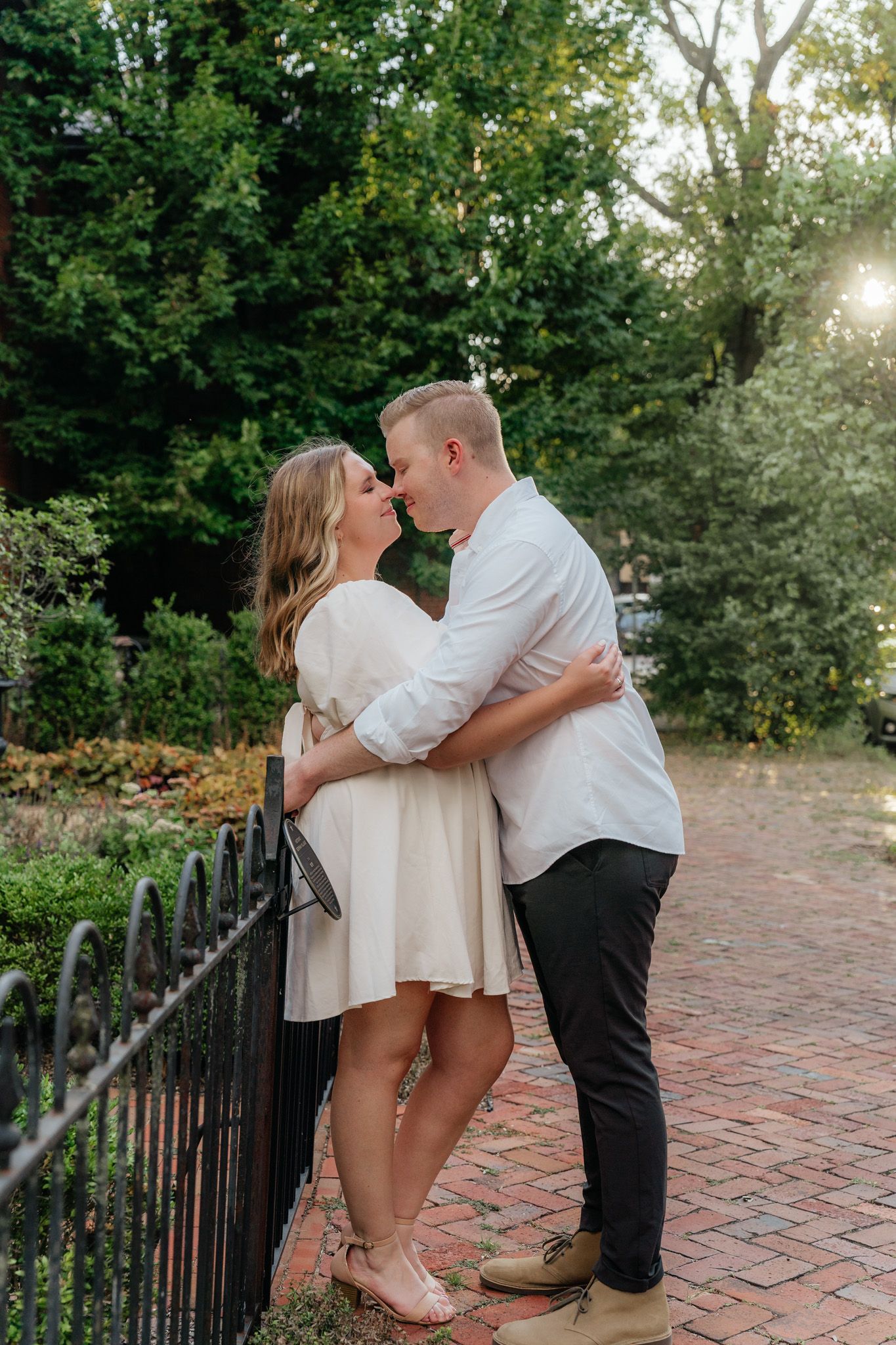 A tender couple shares a romantic moment by a decorative fence on a brick walkway.