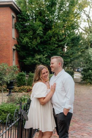 Two people share a joyful moment outdoors by a brick building with green trees in background.