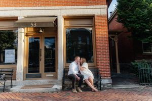 A couple shares an intimate moment on steps of a brick building with the number 53.
