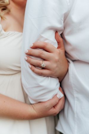 Detail shot of hands and engagement ring against white formal attire.
