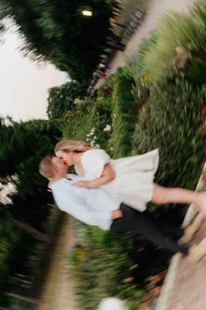 A romantic couple in white clothing twirl together in a garden creating a motion blur effect.