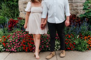 Couple's lower bodies shown standing by vibrant red and pink flowers against a stone wall.