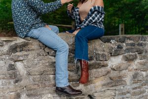 Legs dangling over a stone wall showing brown boots and blue jeans in a casual outdoor setting.