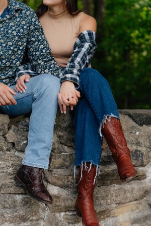 Detail shot of coordinating casual outfits with brown boots and distressed denim on a stone wall.
