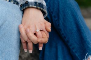 Close-up shot of intertwined hands resting on denim-clad legs.