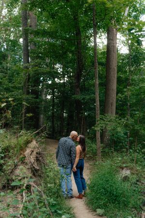A couple sharing an intimate moment on a forest trail surrounded by tall trees.
