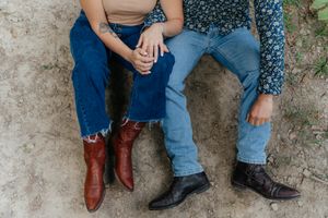 Close-up of two pairs of boots and jeans as couple sits together on forest ground.