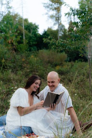 A couple shares laughter while looking at a tablet during their outdoor picnic.