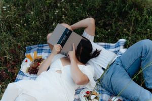 Someone relaxing on a picnic blanket while reading a book outdoors.