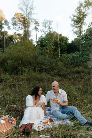 A couple enjoys a romantic picnic on a blanket in a wooded clearing at sunset.