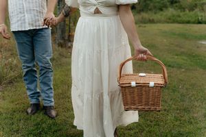 Detail shot of a person holding a wicker picnic basket while wearing a flowing white dress.