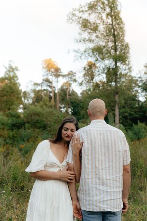 A romantic couple shares a tender moment in a natural outdoor setting with tall trees in the background.