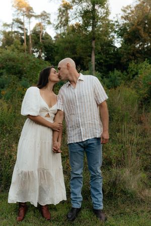 A couple in casual attire shares an intimate moment while standing in a grassy field.