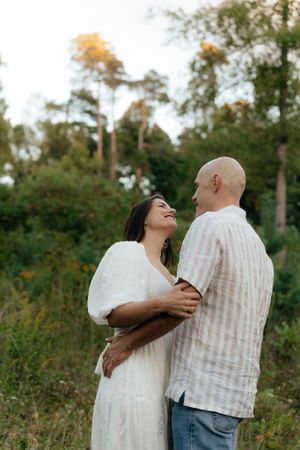 A couple embraces lovingly in a natural outdoor setting with trees and tall grass.