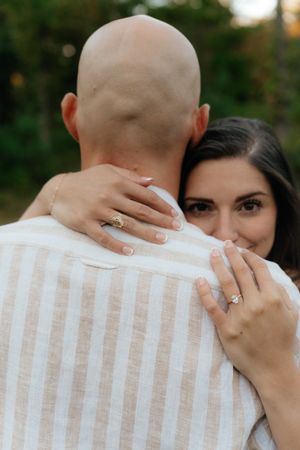 Close-up shot showing hands with engagement ring embracing in an outdoor setting.