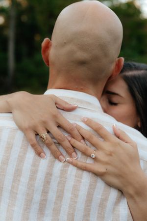 Detailed view of hands with multiple rings embracing against a striped shirt.