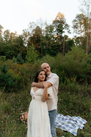 A couple poses together on a picnic blanket in a scenic meadow setting.