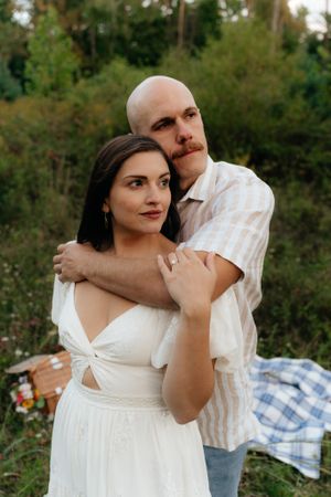 A couple embraces while standing outdoors in coordinated white and striped outfits.