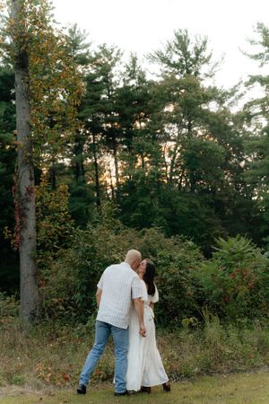A couple shares an intimate moment while walking through an evergreen forest at dusk.